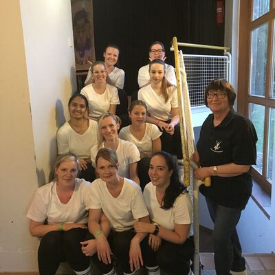 Ein Gruppenfoto des Twirlins Tanzvereins, auf einer Treppe sitzend mt weien T-Shirts. Daneben steht die Trainerin mit einem schwarzen T-Shirt.